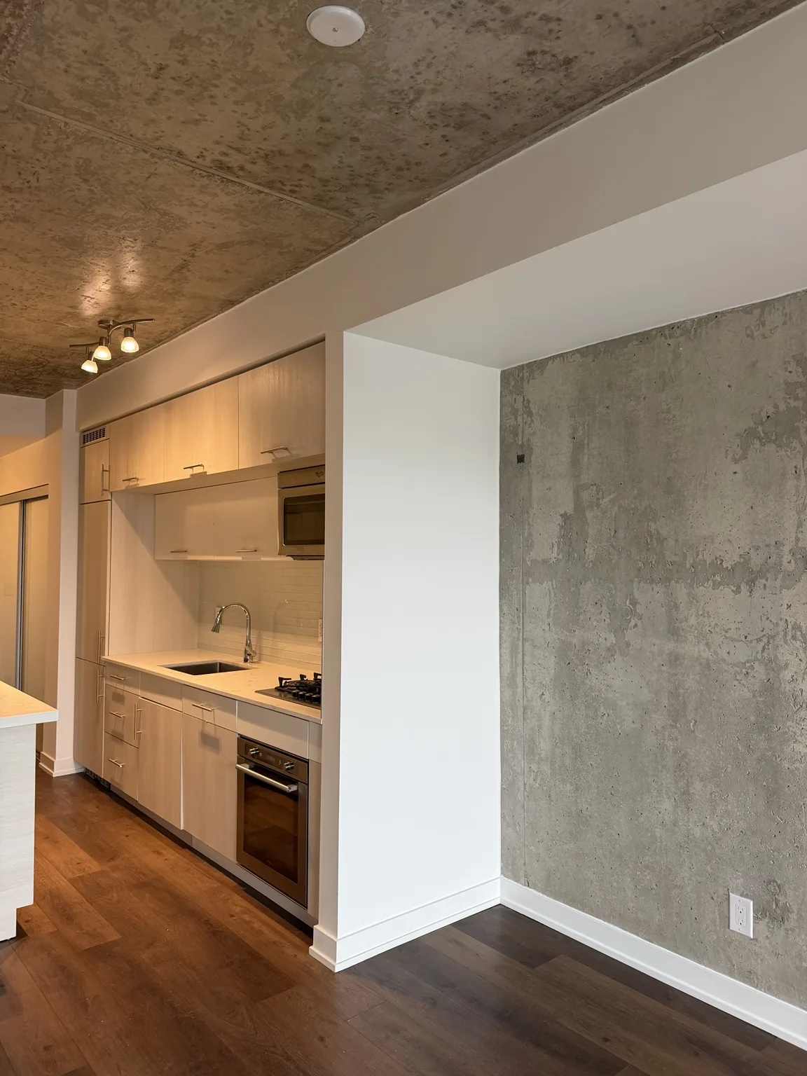 Freshly repainted condo kitchen and living area with exposed concrete feature wall
