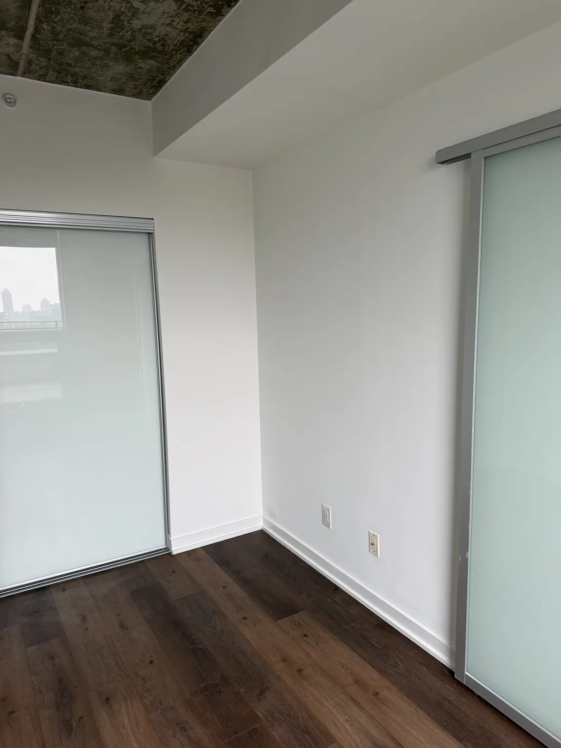 Condo bedroom corner with freshly painted walls, baseboards and frosted glass closet doors